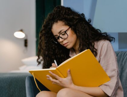 A woman writing in a large yellow notebook while journaling in addiction recovery