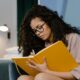 A woman writing in a large yellow notebook while journaling in addiction recovery